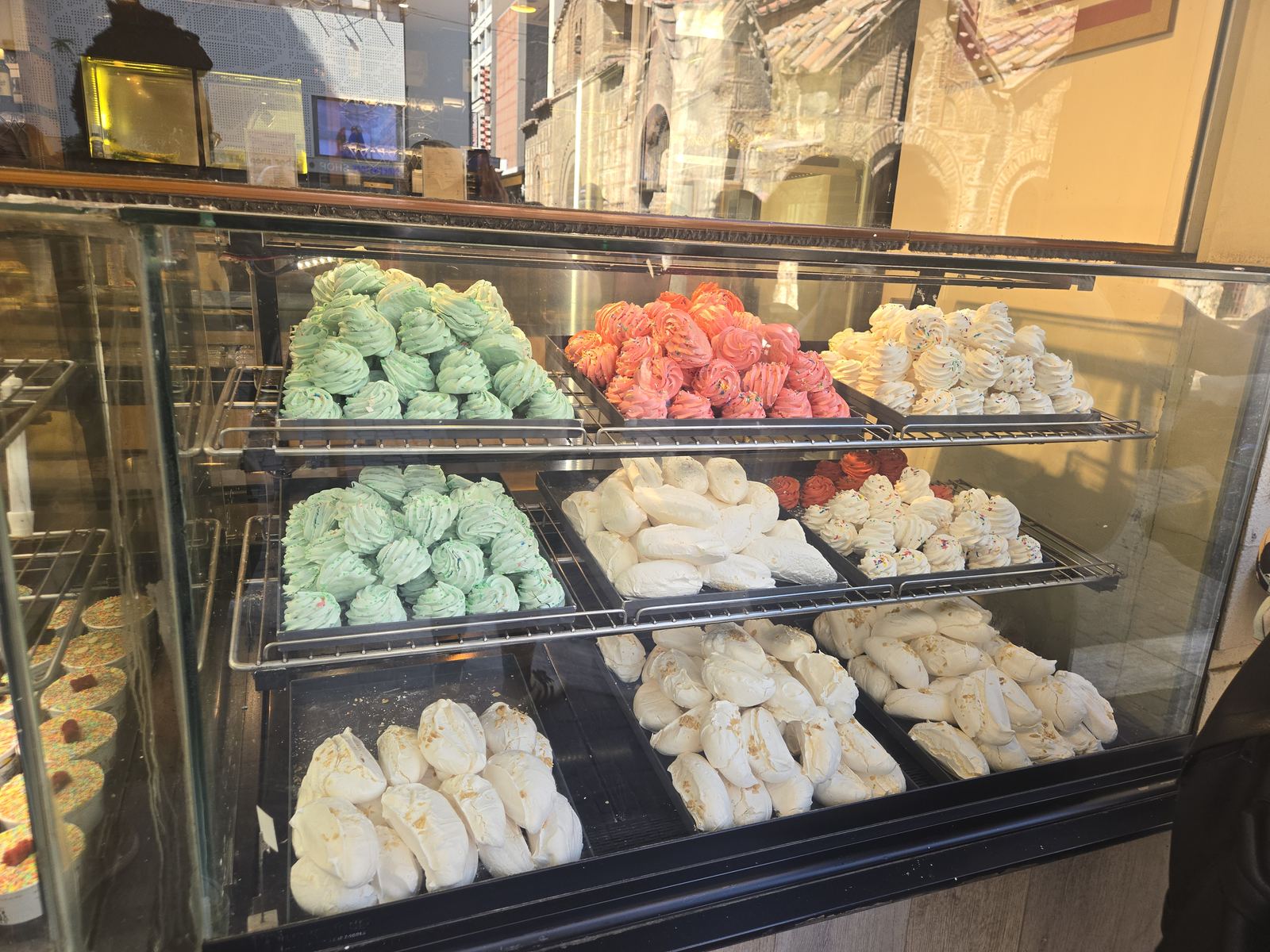 A bakery window in Athens filled with trays of pastel meringues and pastries