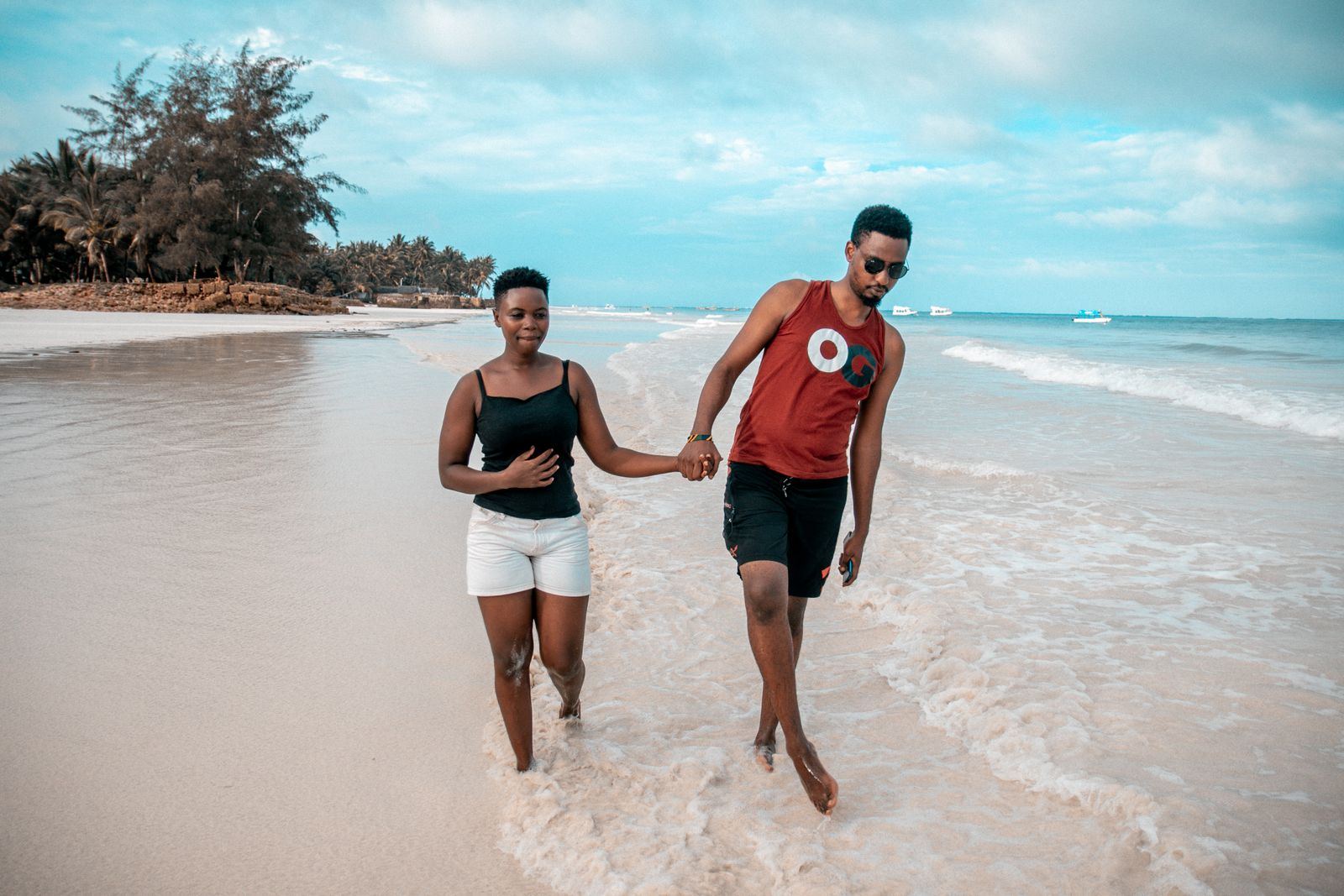 A young couple walking hand in hand along the shoreline on a tropical beach